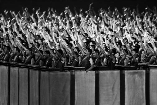 Alternative Text</h5><p>Large group of over 100 similarly dressed western asian men in a stadium stand all raising their right arms and shouting.
